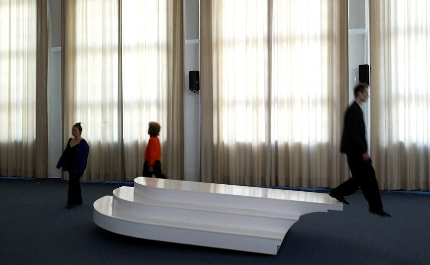 3 performers keep crossing an interactive sea-saw sculptural interface in a choreographed manner, with different speeds and attitudes, sometimey apruptly changing directions. The sculpture has a rectangular, platform like shape, with three steps at the sides.