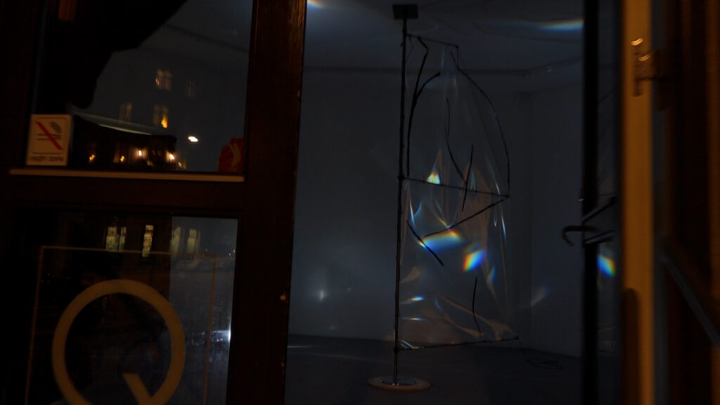 View into a round gallery space with a transparent sail installed in the middle of it between the ceiling and the floor, with light broken down to its spectral colours projected on it. 