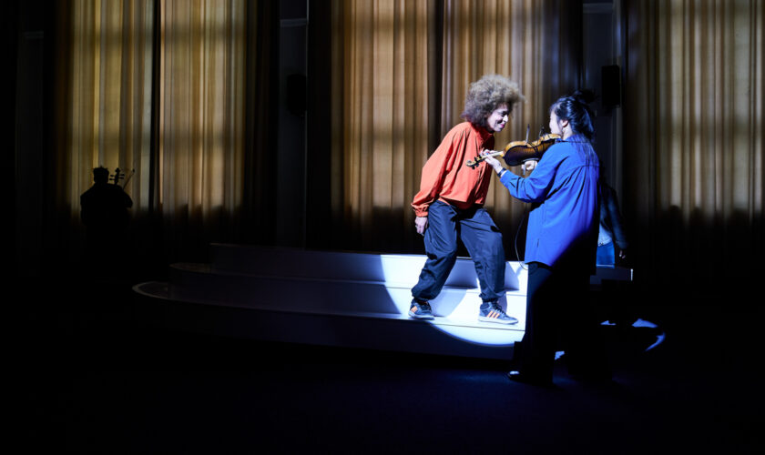 Valerie Renay stands on an interactive sculptural platform facing violinist Sung Mi Marina Kim, illuminated by a concentrated spotlight during Axis.