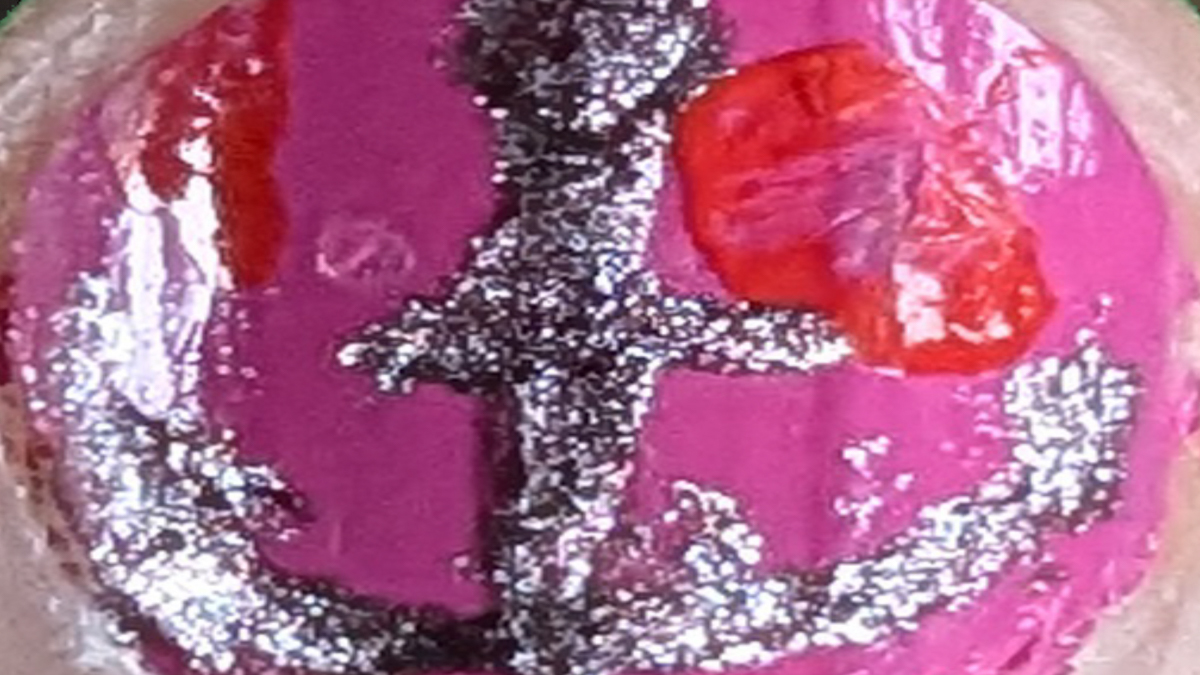 Macro shot of a silver anchor painted on a pinkie finger with pink foundation.