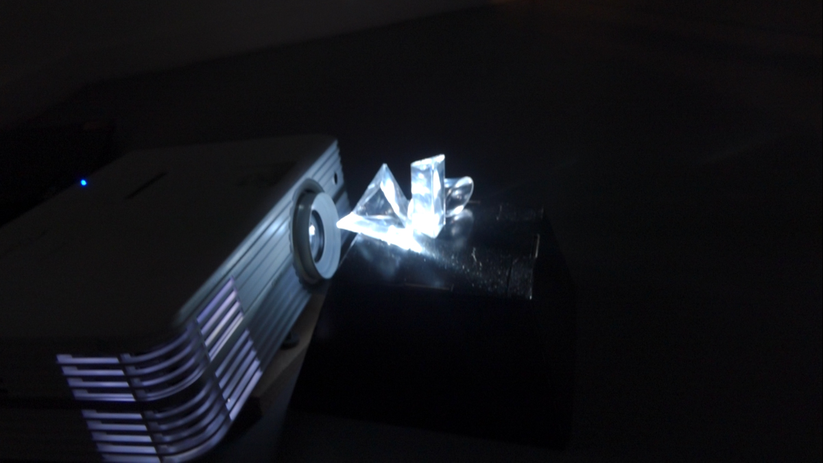 Projector projecting an animated white circle through glass prisms placed in front of the lense.
